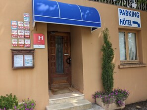 Entrada de hotel con un toldo azul, puerta de madera y un letrero que indica un estacionamiento.