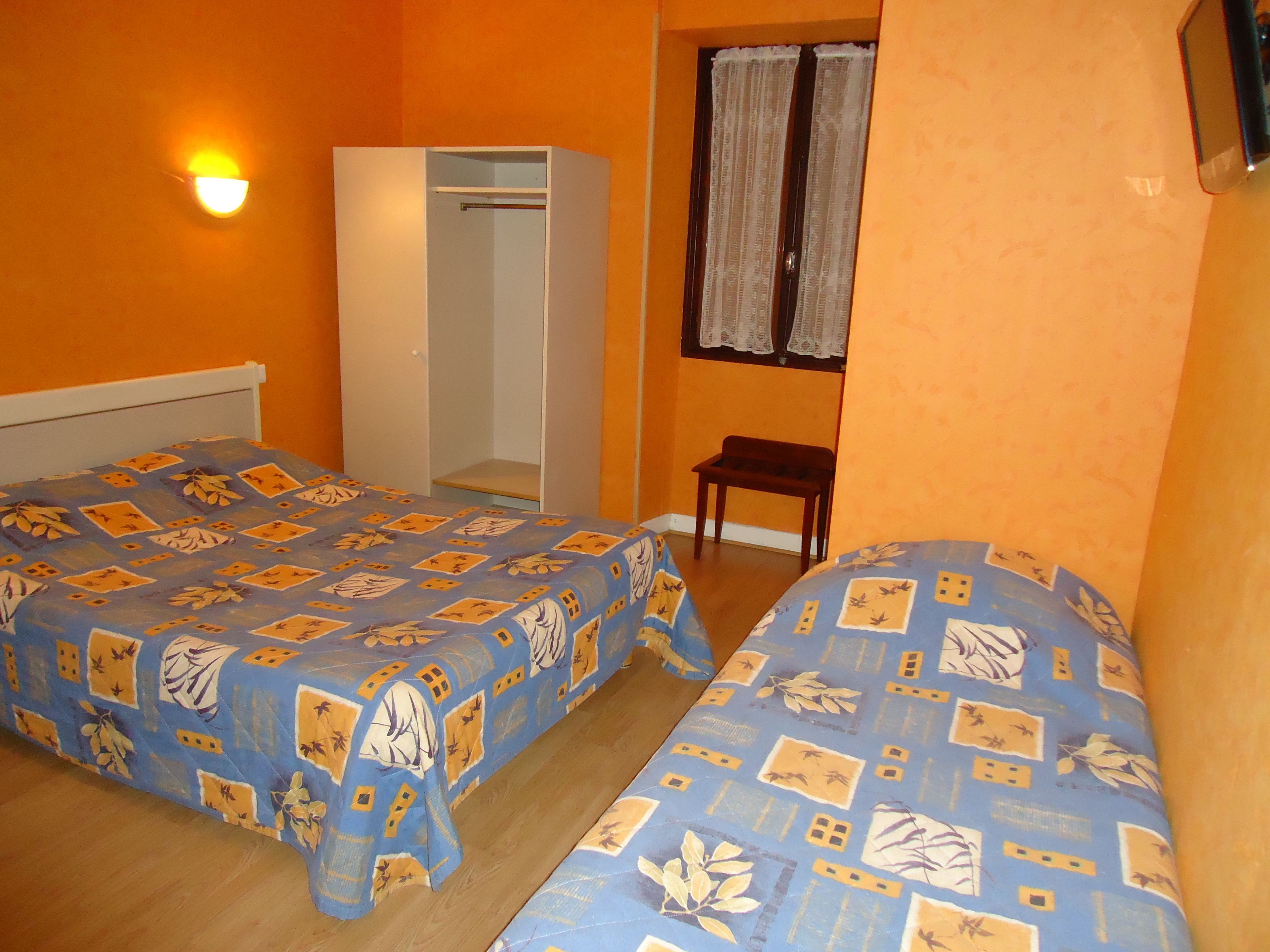 A room with two beds, a wardrobe, a small table, and a window with curtains.