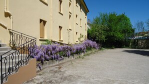 Un edificio de fachada color crema, con múltiples ventanas y un sendero de concreto con flores púrpuras.