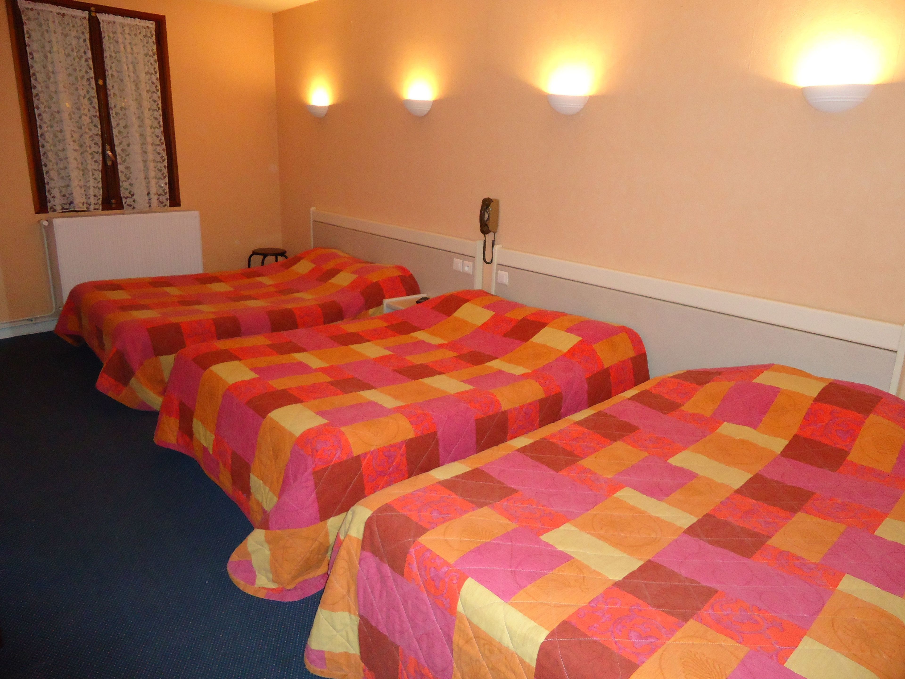 A hotel room with three single beds, a telephone, and a window with curtains.