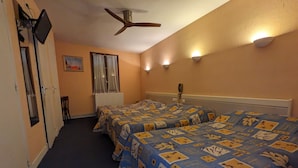Habitación de hotel con dos camas, ventilador de techo, radiador, un cuadro en la pared y una ventana con cortinas.