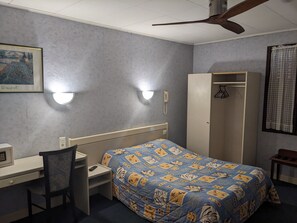 Una habitación de hotel con cama, escritorio, silla, armario y ventilador de techo.