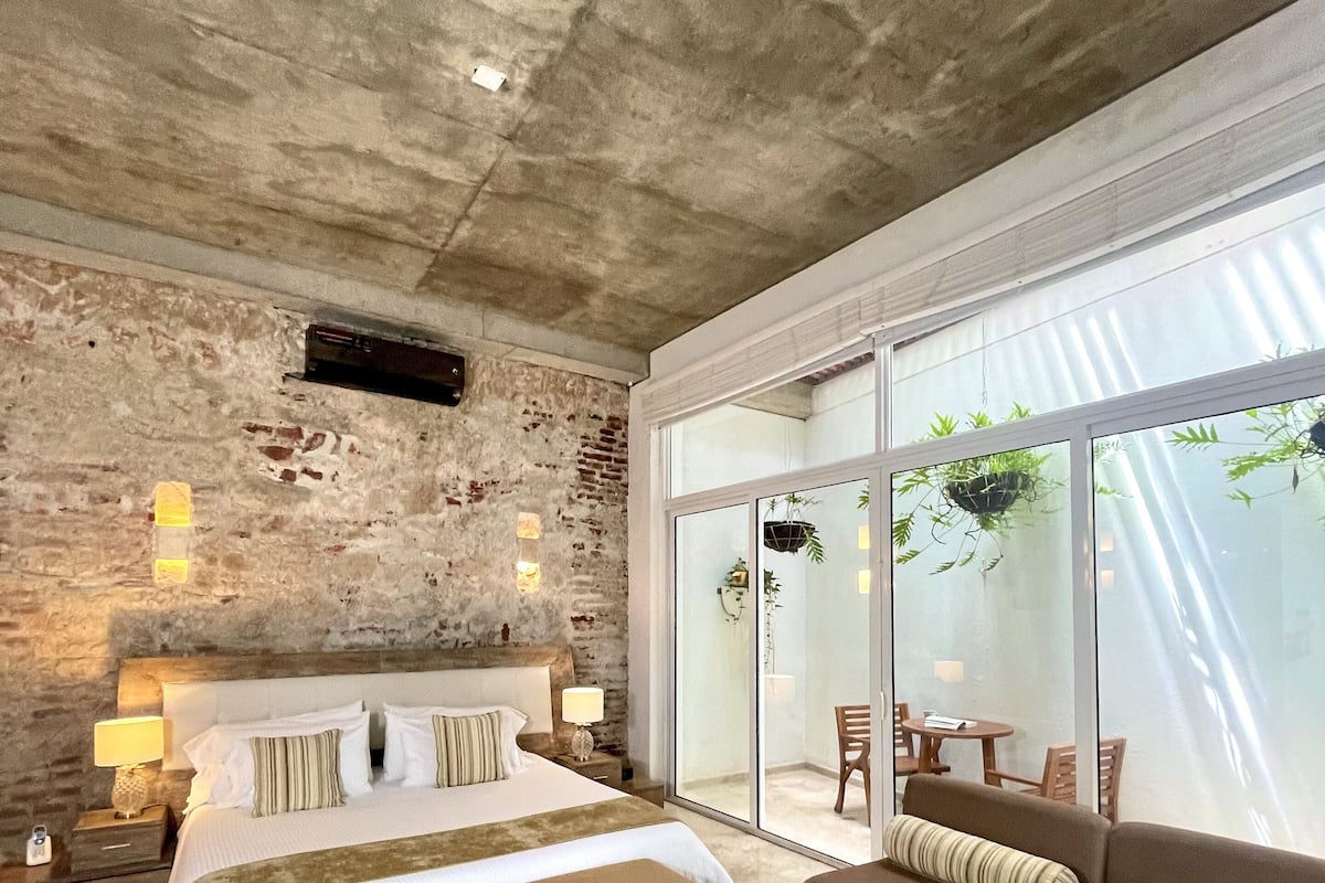 Un dormitorio moderno con una cama grande, un sofá y un balcón con plantas.