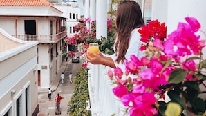 A balcony with pink flowers, a person holding a drink, and buildings in the background. - Casa Claver Loft Boutique Hotel (Cartagena)