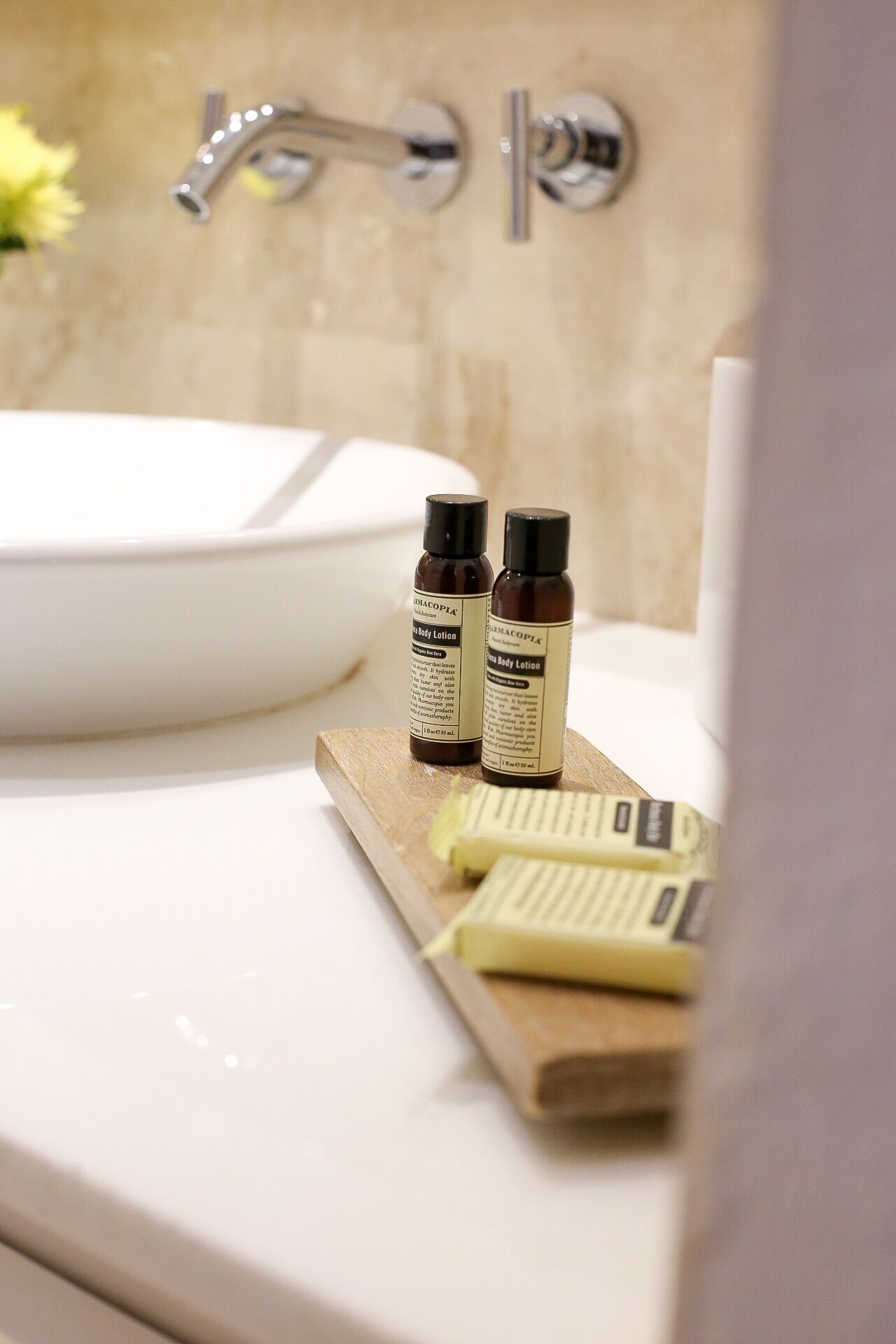 Un baño con un lavamanos blanco, dos botellas de crema corporal y una pastilla de jabón sobre una bandeja de madera.