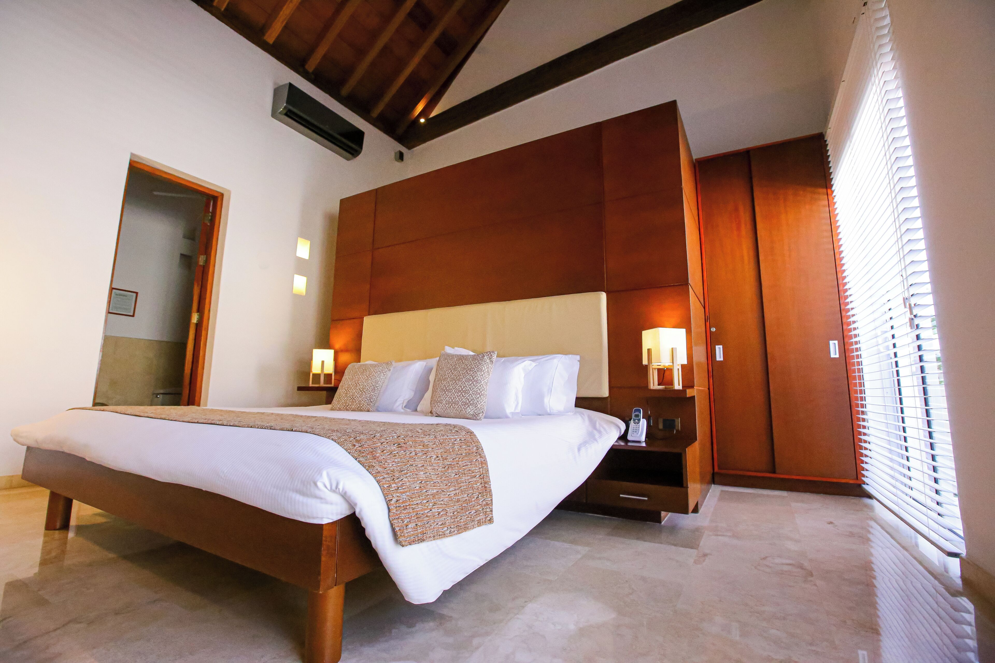 Quarto moderno com cama grande, cabeceira de madeira, luminárias laterais e um espelho.