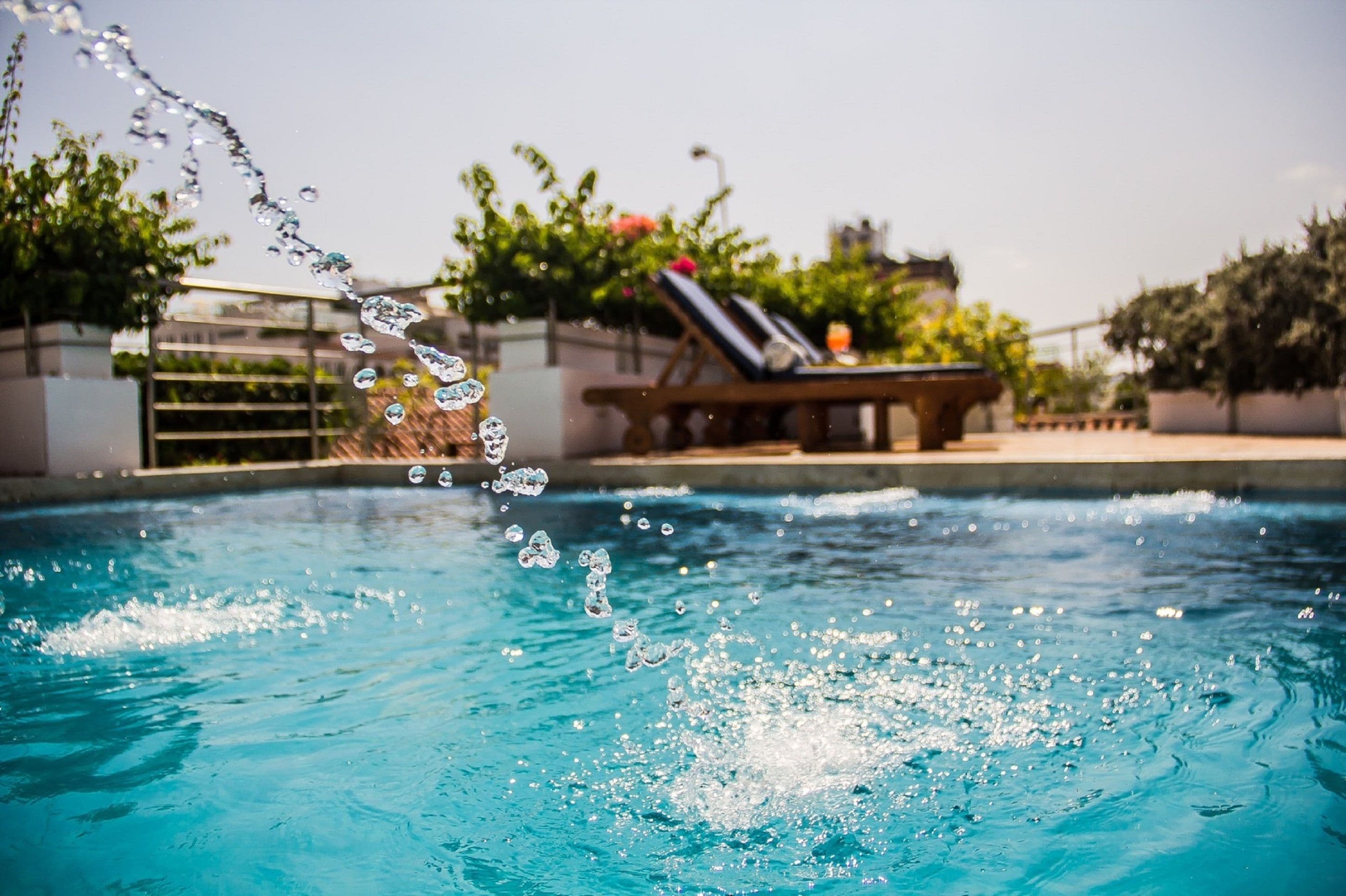 A swimming pool with water splashing, a lounge area with sun loungers, and potted plants.