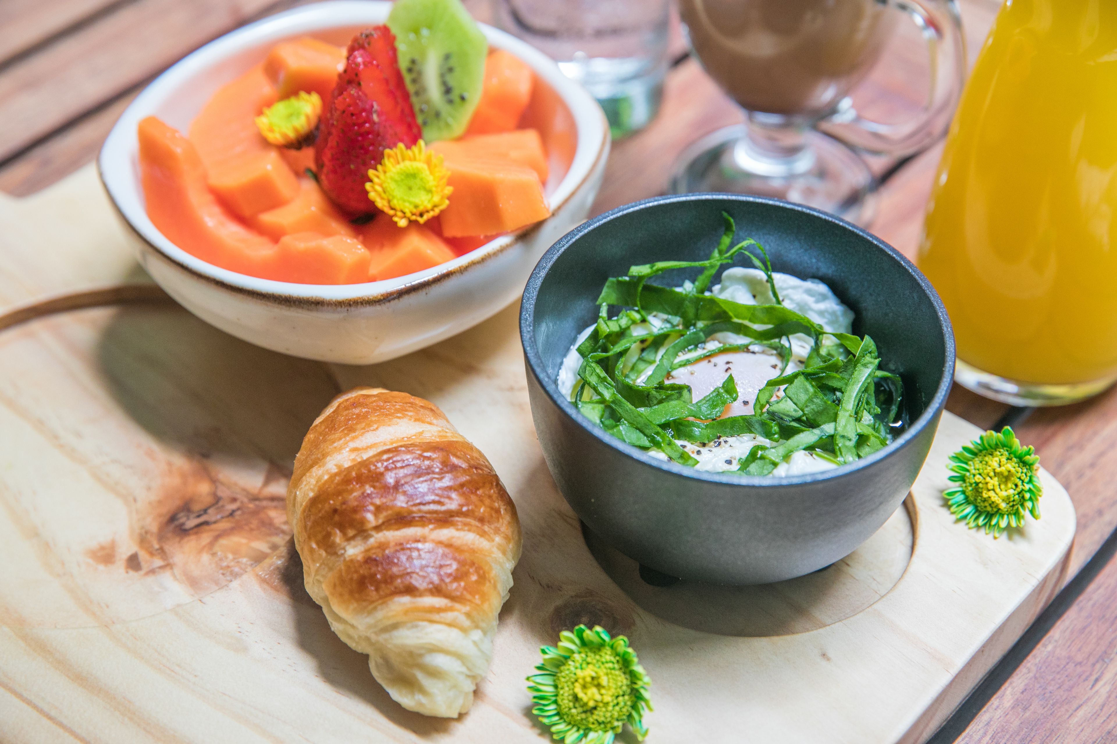 A meal with a croissant, a bowl of soup with vegetables, and a glass of juice on a wooden table.