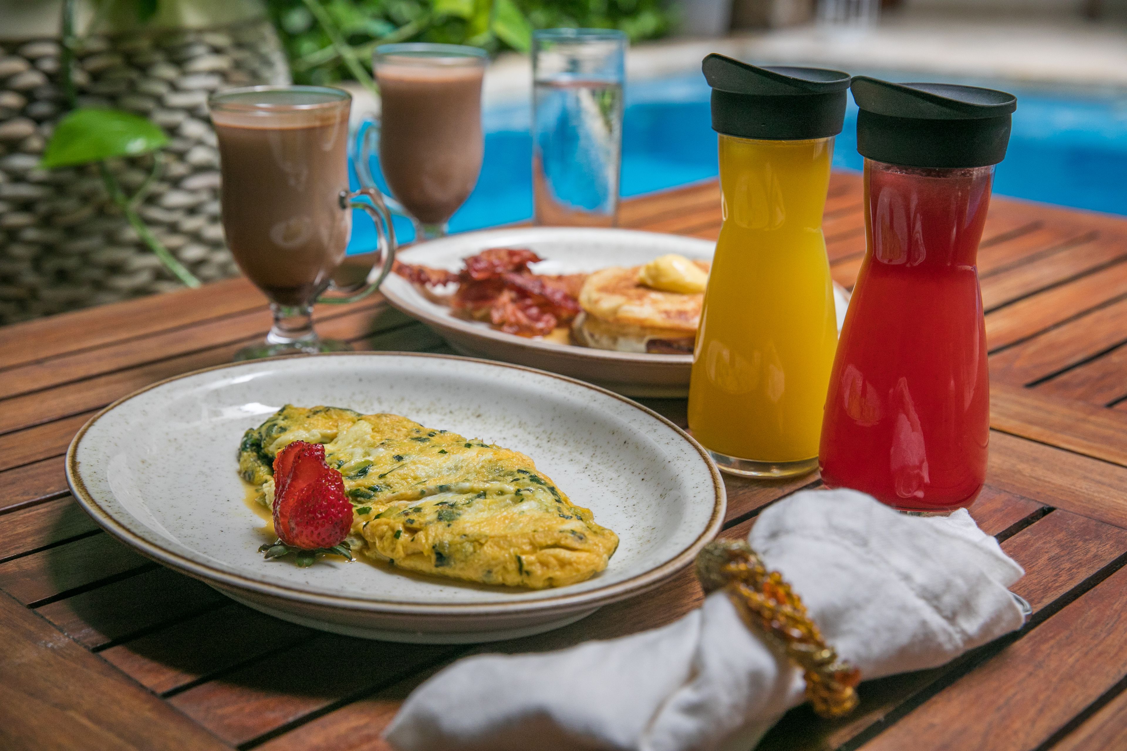 Una mesa de madera junto a una piscina con un plato de comida, un vaso de leche y dos botellas de jugo.