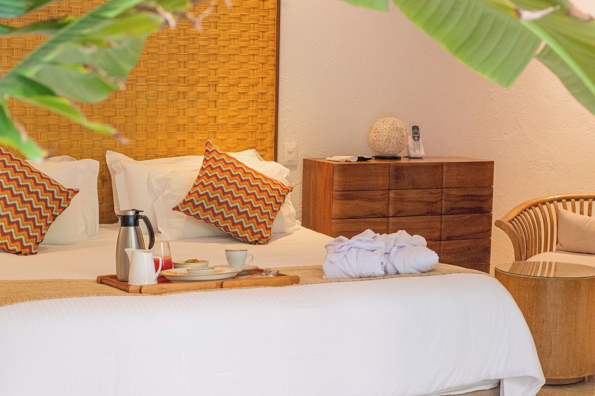 Una habitación de hotel ordenada con una cama grande, una mesita de noche de madera, una silla y un panel decorativo en la pared.
