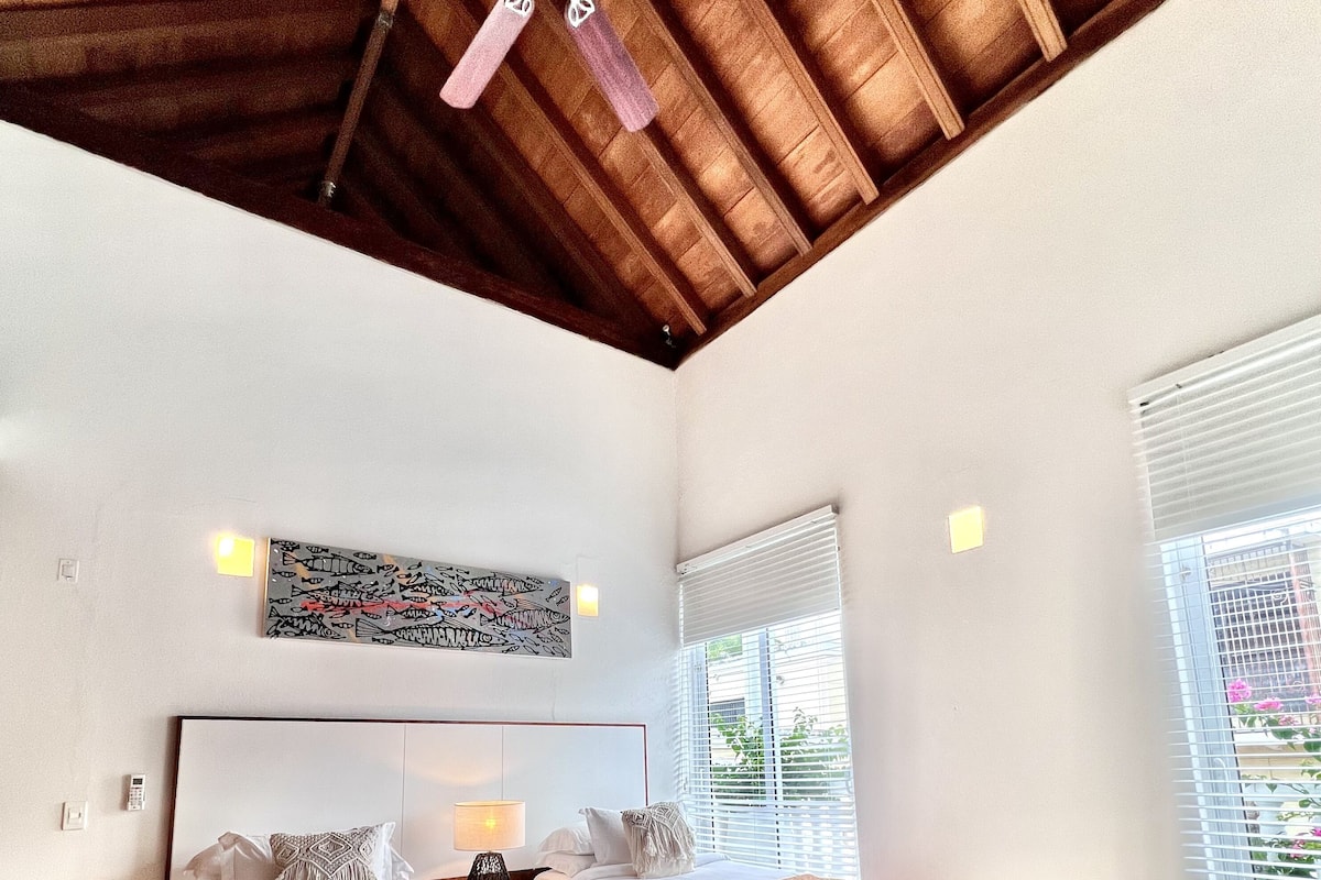 Un dormitorio con dos camas, un ventilador de techo, una ventana con persianas y una obra de arte colgada en la pared.