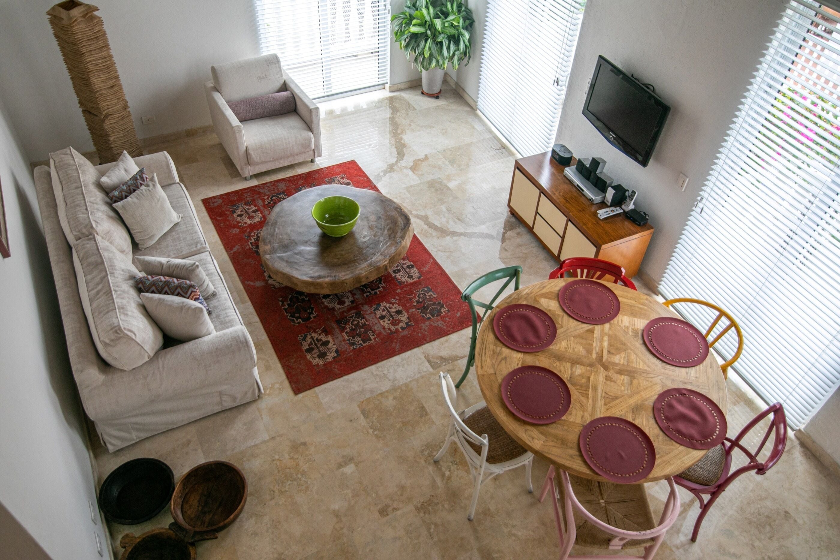 A living room with a sofa, a coffee table, a dining table with chairs, a TV, and a plant.