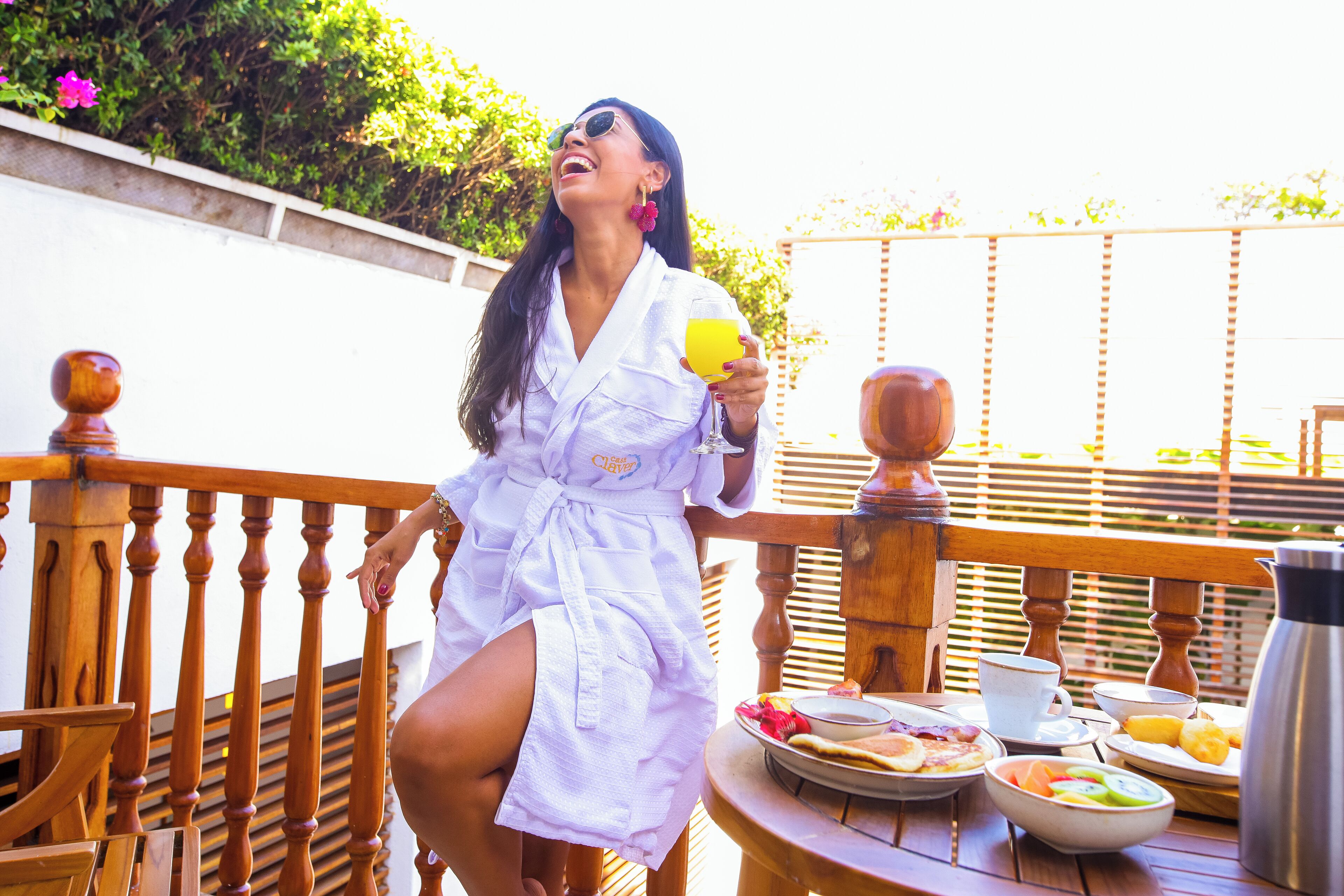 A person in a white robe sitting on a wooden deck with a table set with breakfast items.