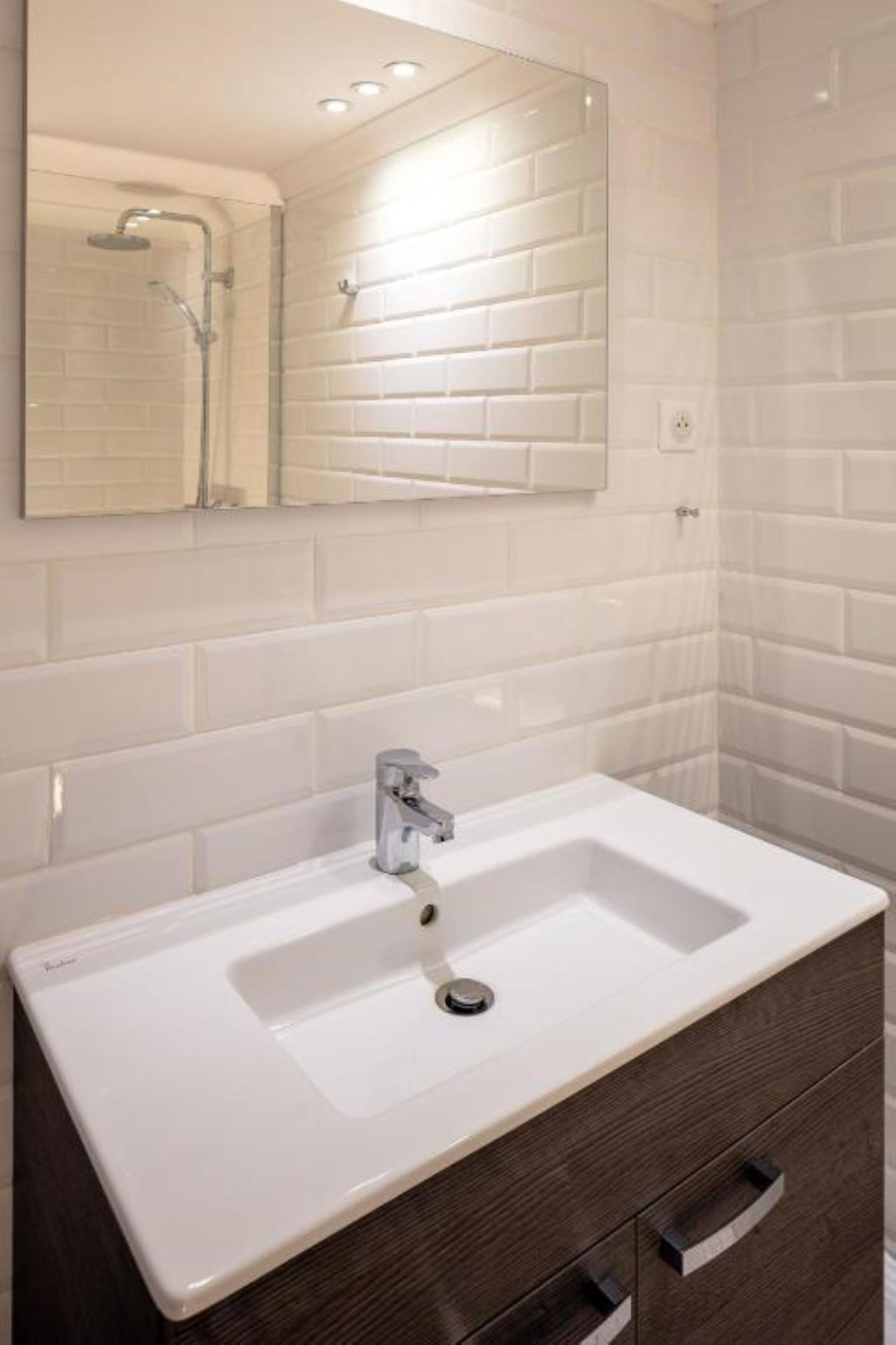 Un baño con lavamanos blanco, tocador de madera oscura y espejo sobre el lavamanos.