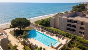 A pool with a view of the beach and ocean, surrounded by greenery and a building with multiple floors. - Résidence Marina Bianca (Santa-Lucia-di-Moriani)