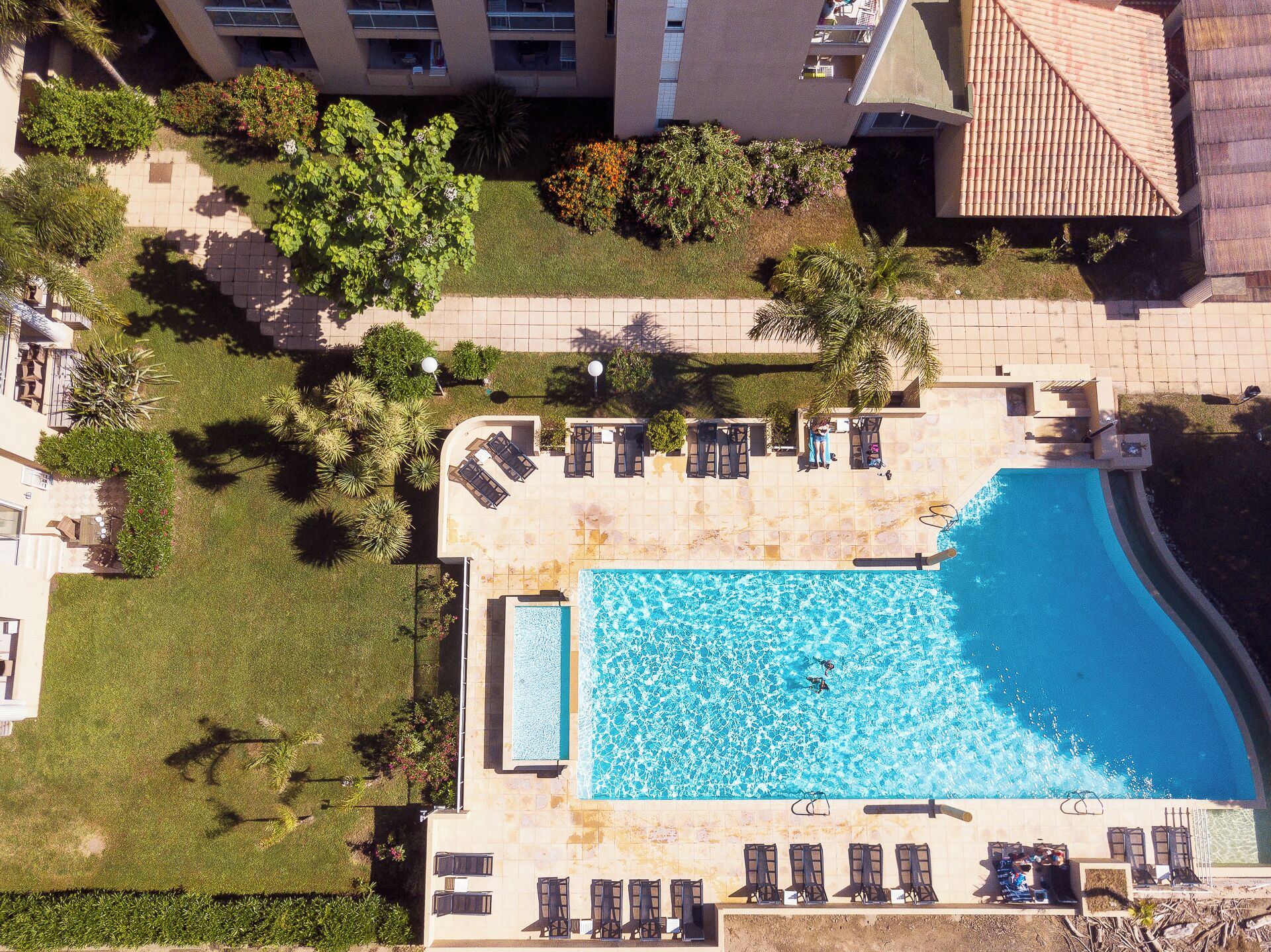 Vista aerea di un hotel con piscina, lettini da sole e giardino curato.