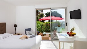 A hotel room with a bed, a desk with a fruit bowl, a red umbrella, and a TV on the wall. - Résidence Marina Bianca (Santa-Lucia-di-Moriani)