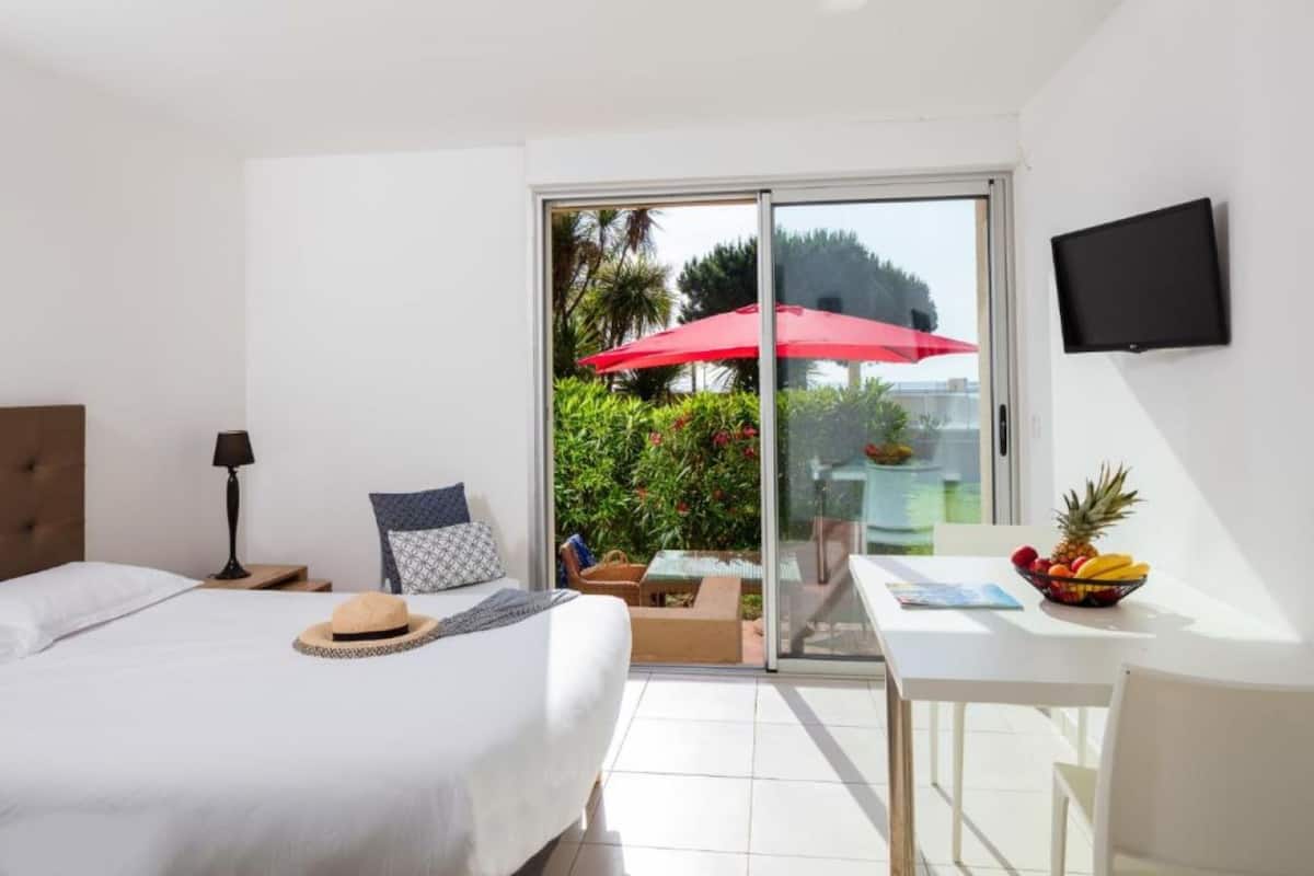 A hotel room with a bed, a desk with a fruit bowl, a red umbrella, and a TV on the wall.