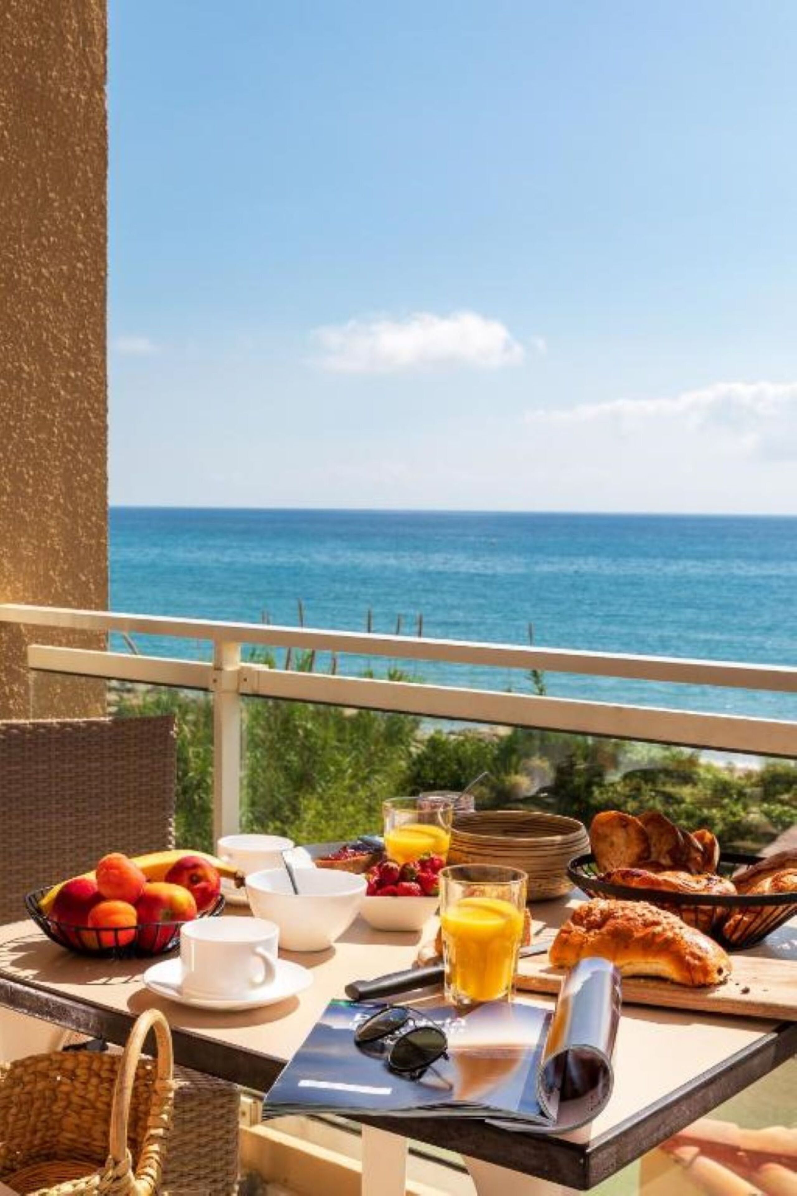Taula de petit esmorzar amb fruita, suc i pastissos, amb vista al mar.