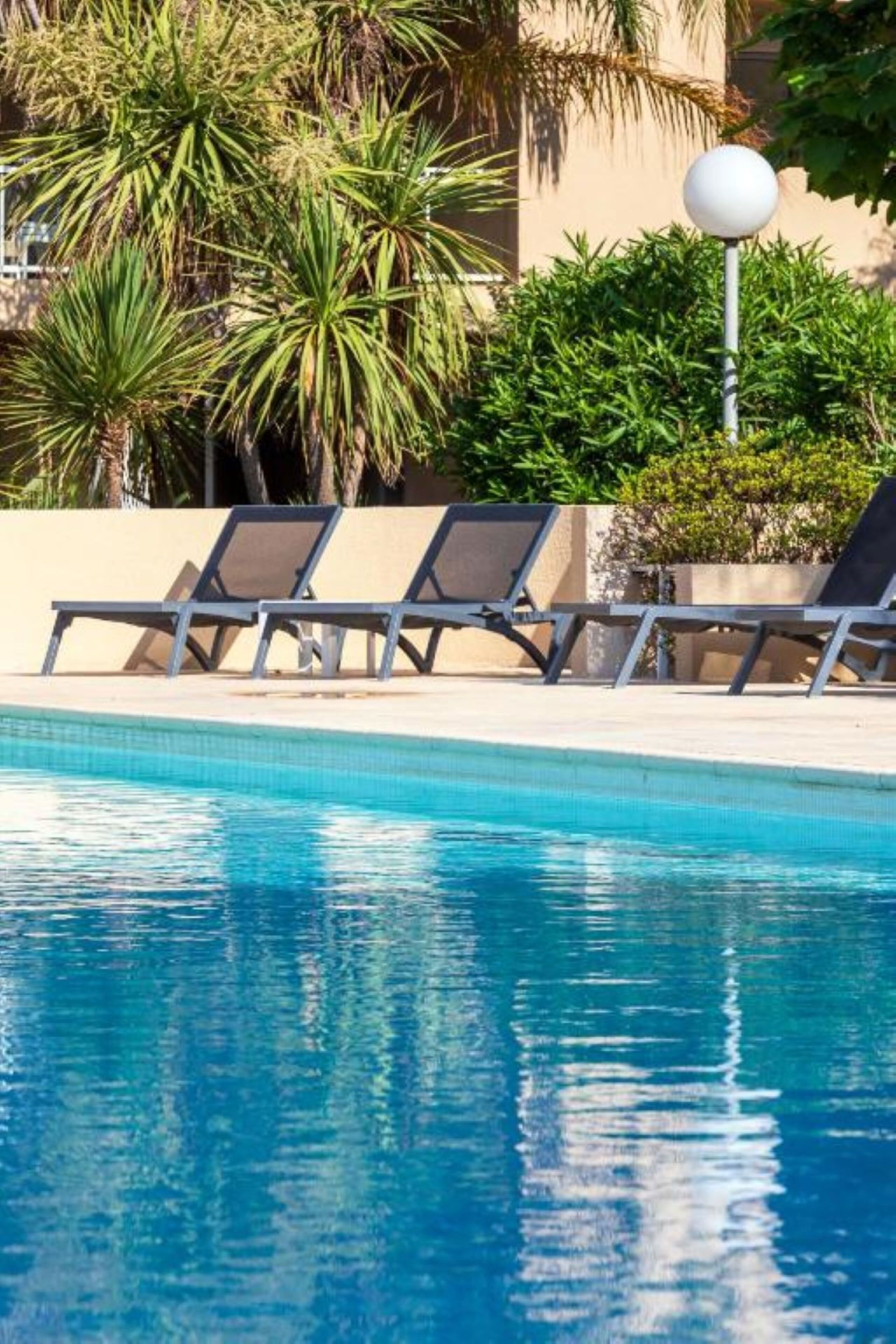 A pool with clear blue water, surrounded by lounge chairs and palm trees.