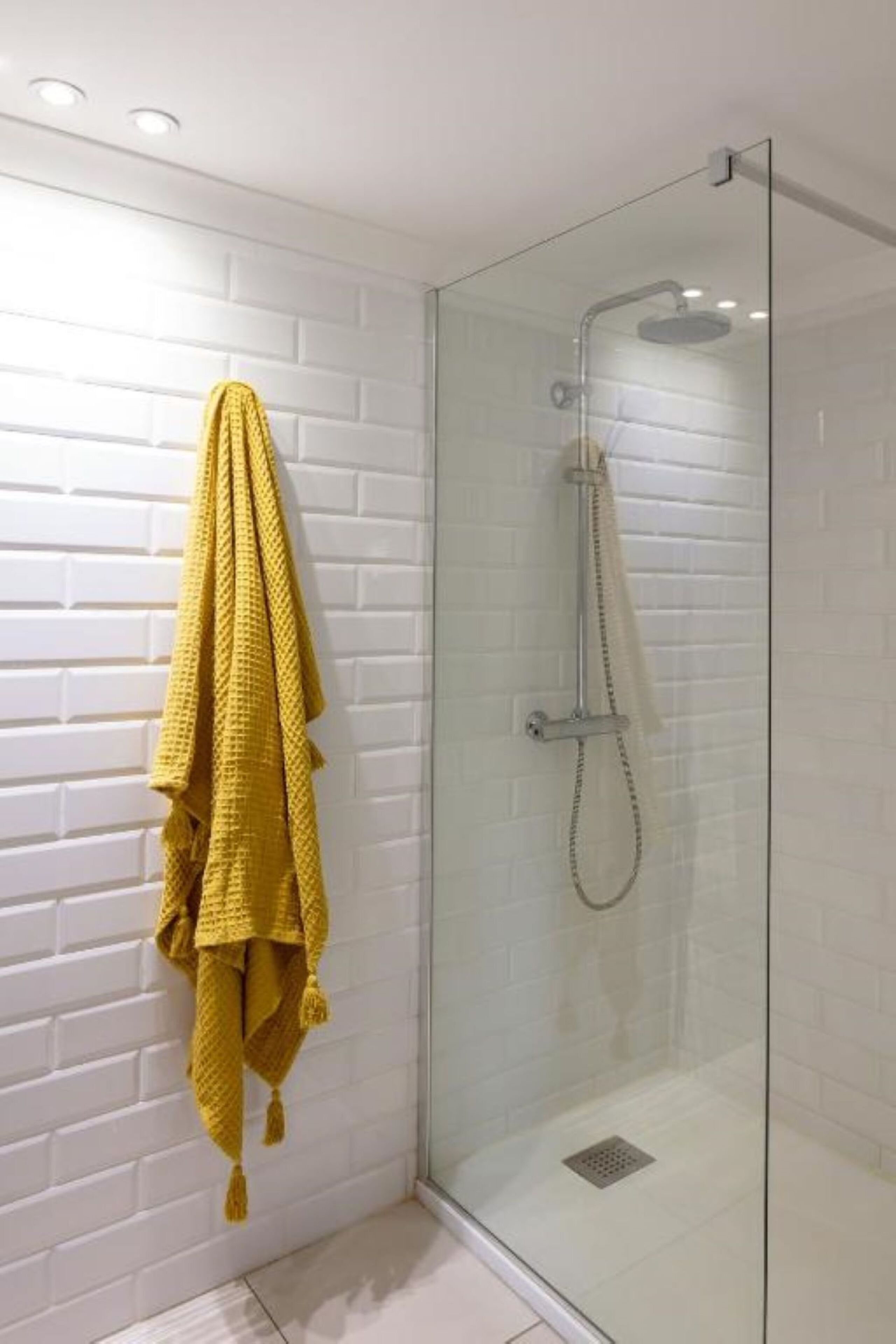 Eine gläserne Dusche mit einer weißen Backsteinwand und einem gelben Handtuch an der Wand.