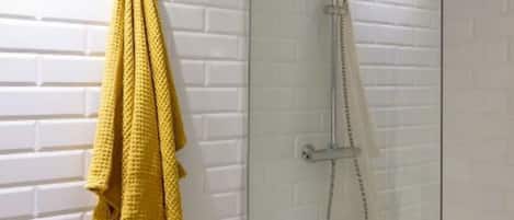 Eine gläserne Dusche mit einer weißen Backsteinwand und einem gelben Handtuch an der Wand.