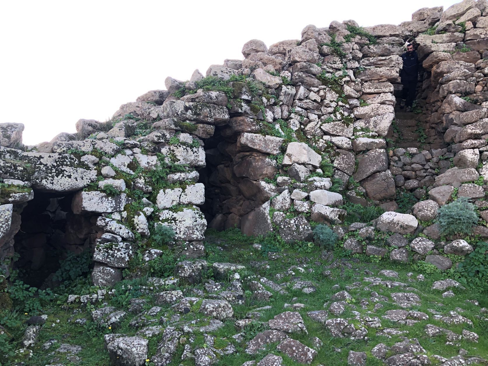 A rocky landscape with a cave entrance and a person standing inside.