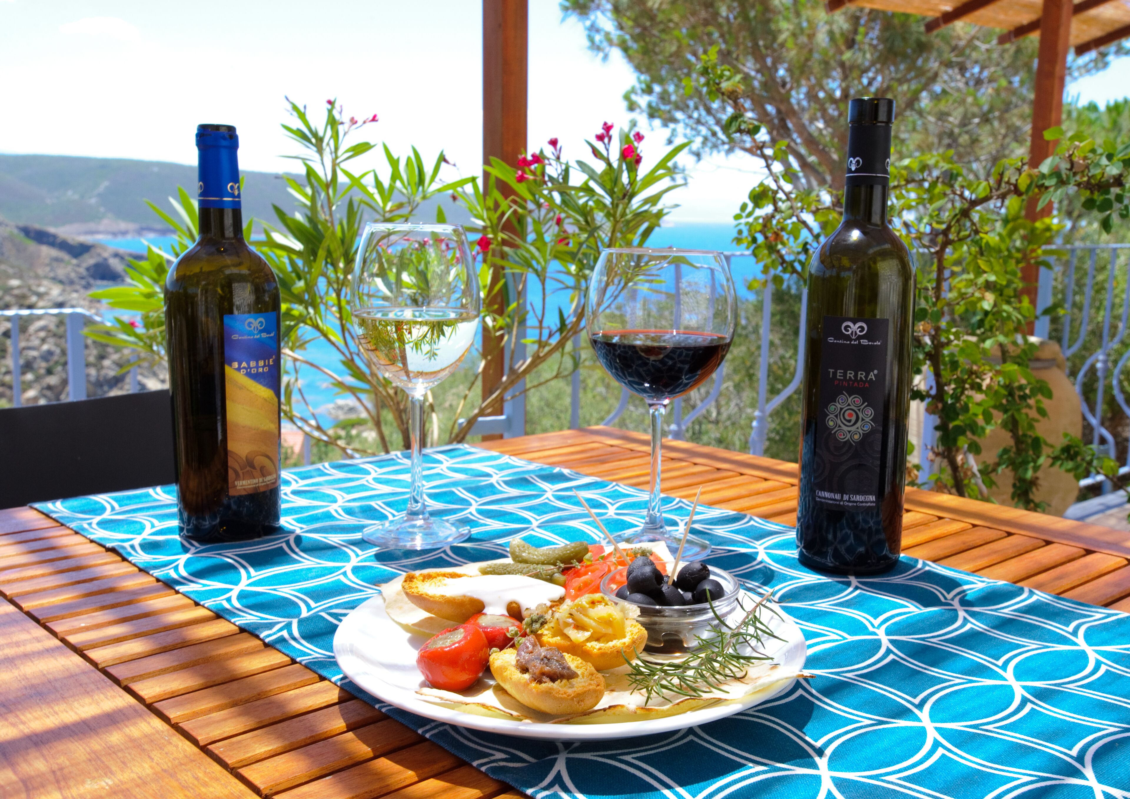 A table with a blue patterned tablecloth, two wine bottles, two wine glasses, and a plate of food.