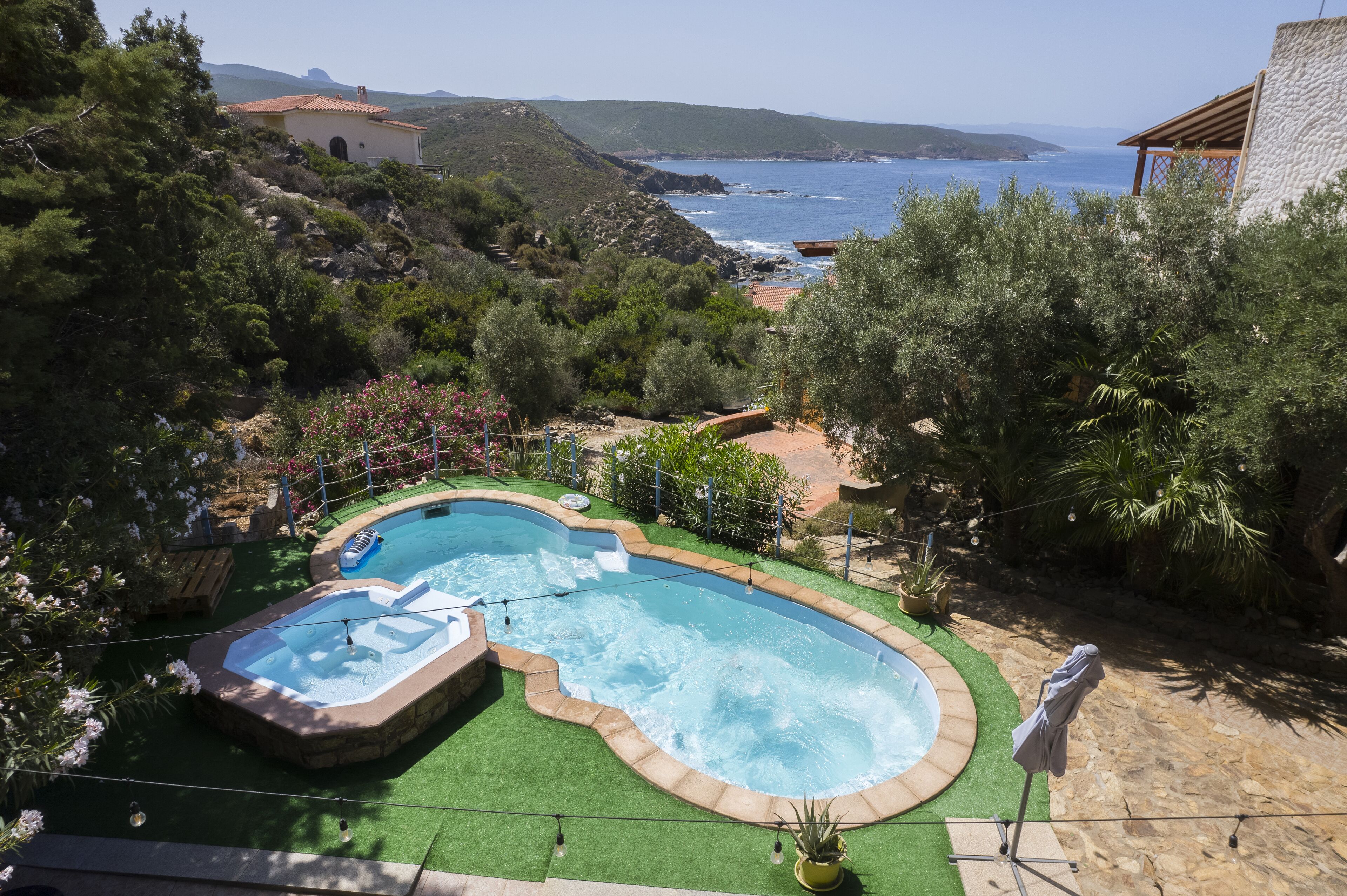A swimming pool with a hot tub, surrounded by greenery and a view of the sea.