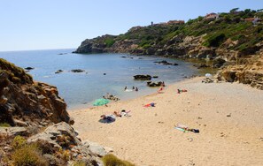 A coastal beach with rocky cliffs, clear blue water, and a sandy shore with people sunbathing and swimming. - Villa Belfiori (Arbus)