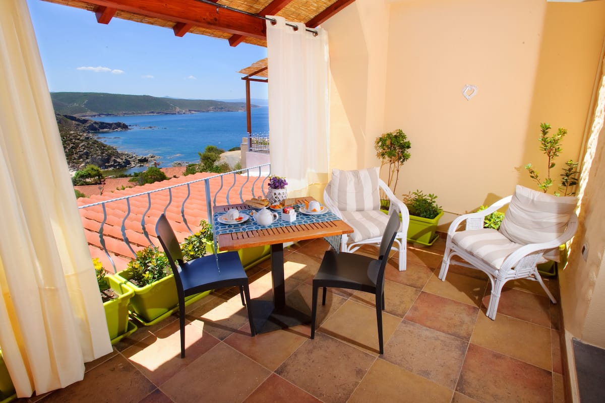 A balcony with a table set for two, two chairs, and potted plants.