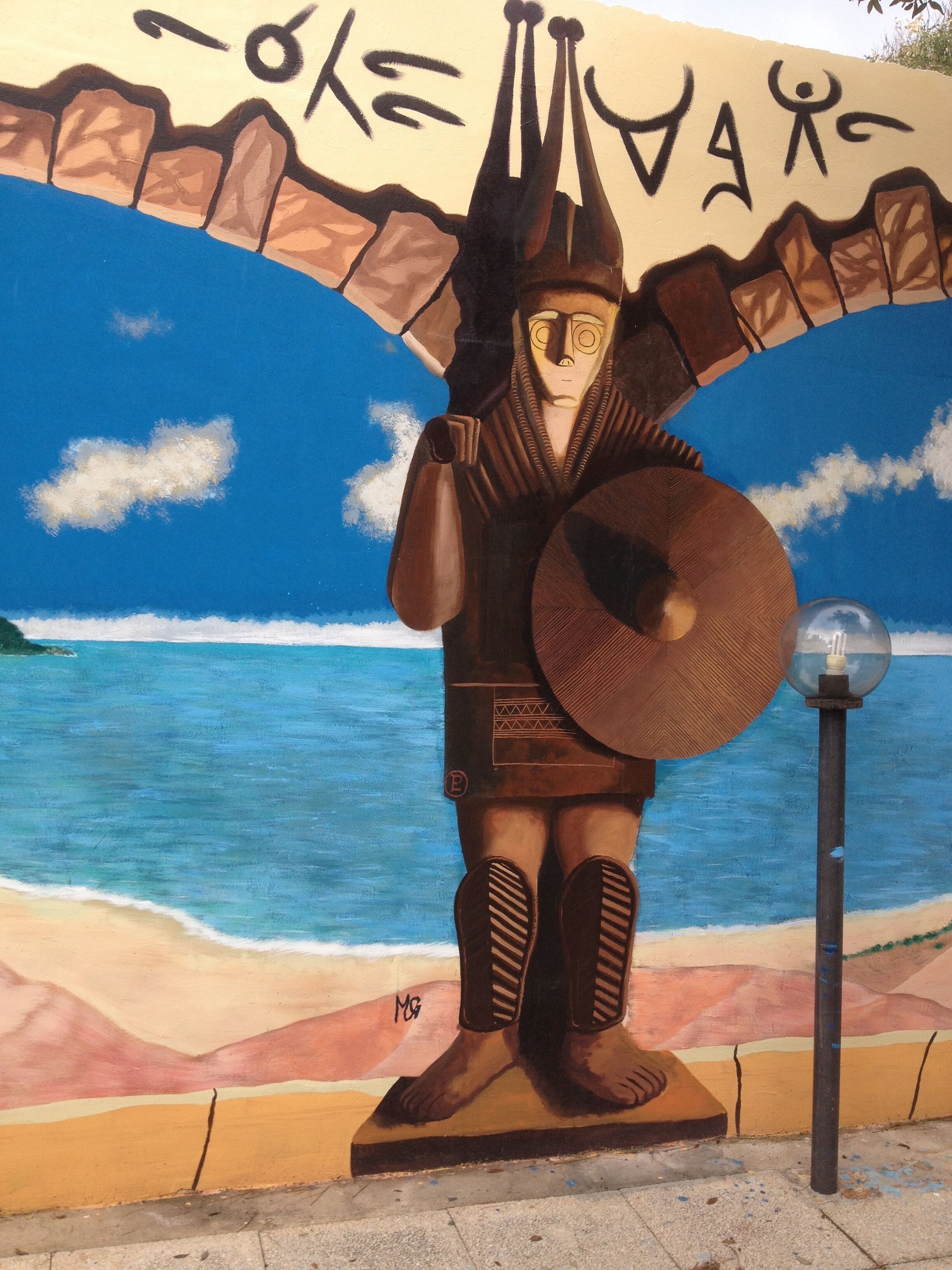 Un murale raffigura una figura che regge uno scudo e una spada, con una spiaggia e l'oceano sullo sfondo.