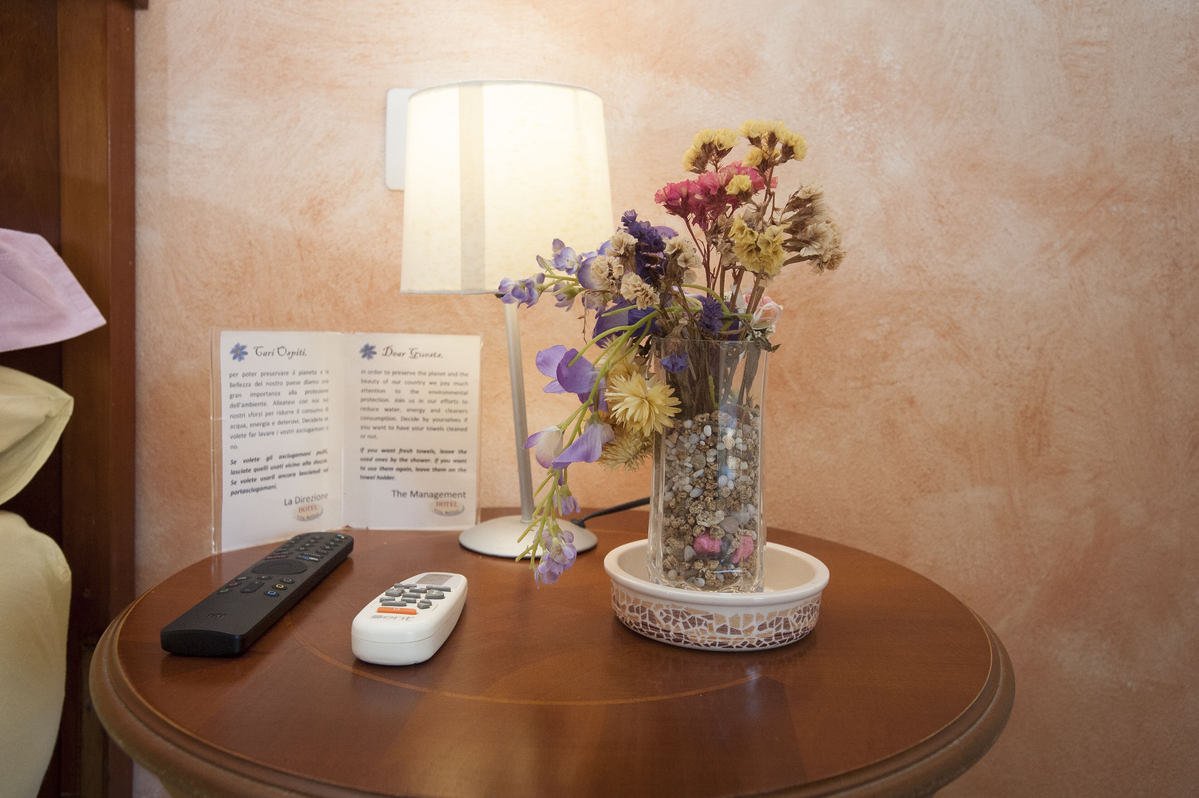Una mesa con un jarrón de flores, un control remoto y un cartel con texto.