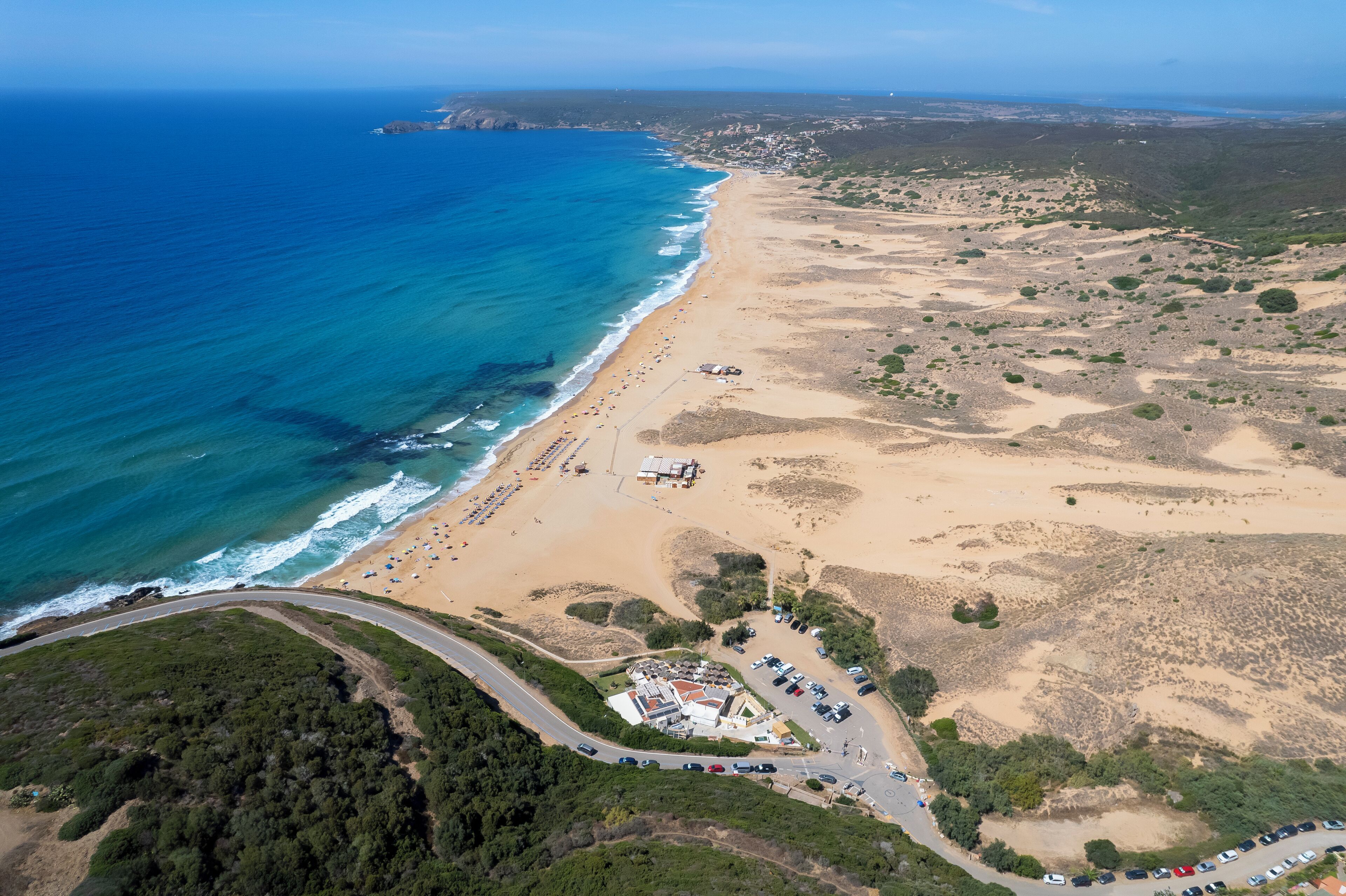 An aerial view of a coastal area with a beach, parking lot, and a building complex.