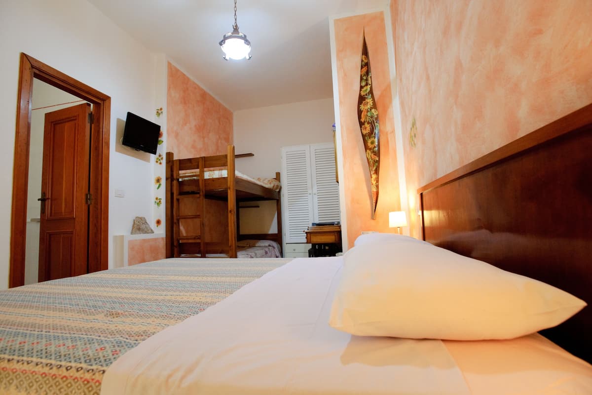 A bedroom with a bunk bed, a wooden wardrobe, a television on the wall, and a ceiling light.