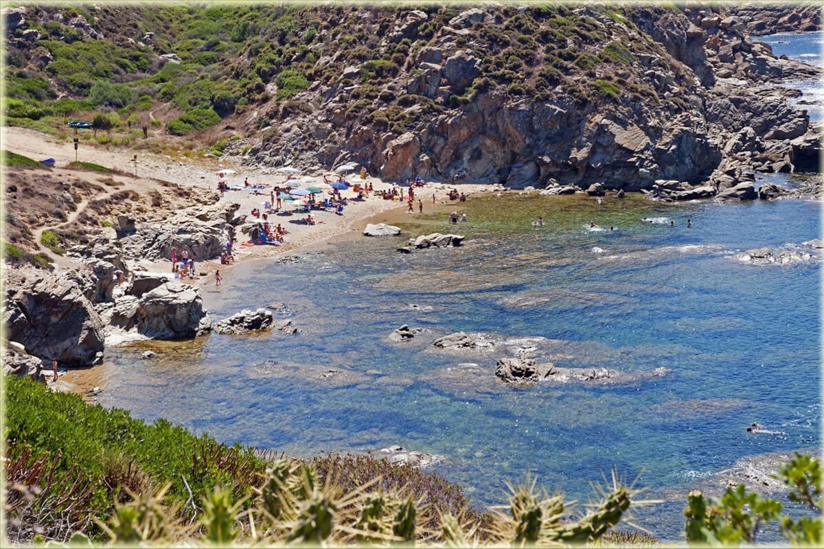 A rocky beach with clear water and people sunbathing.