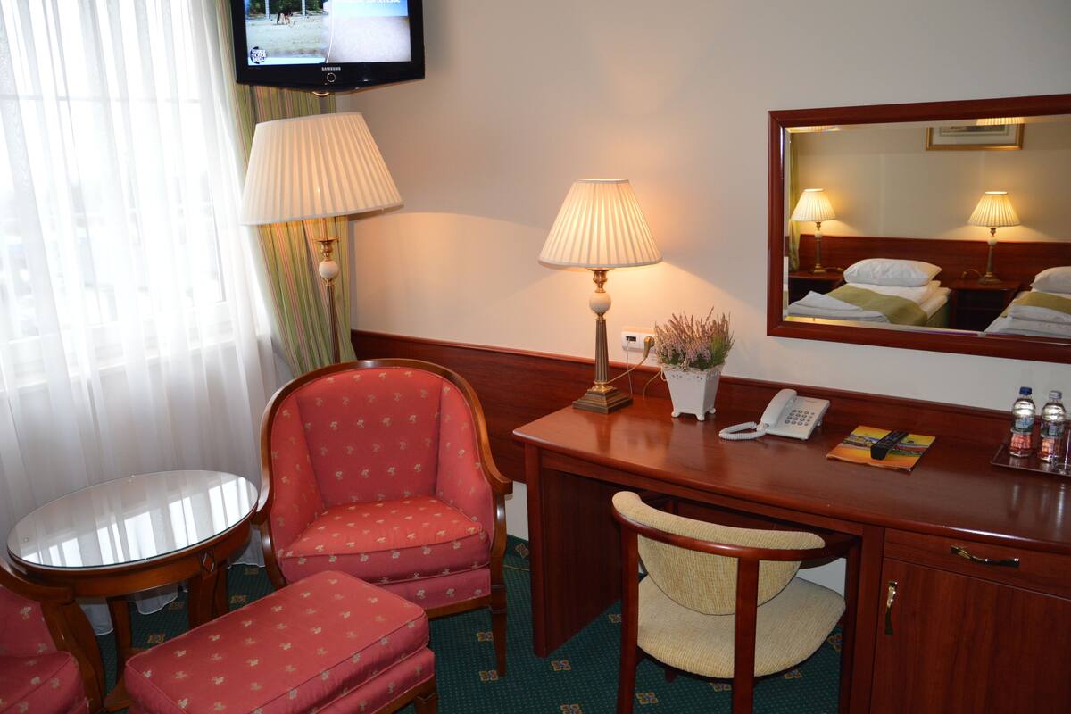Habitación de hotel con un escritorio de madera, dos lámparas, un televisor, un espejo, un teléfono y una mesita.