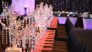 Una larga mesa con servilletas rojas y árboles decorados con cristales, sobre un fondo de luces desenfocadas.