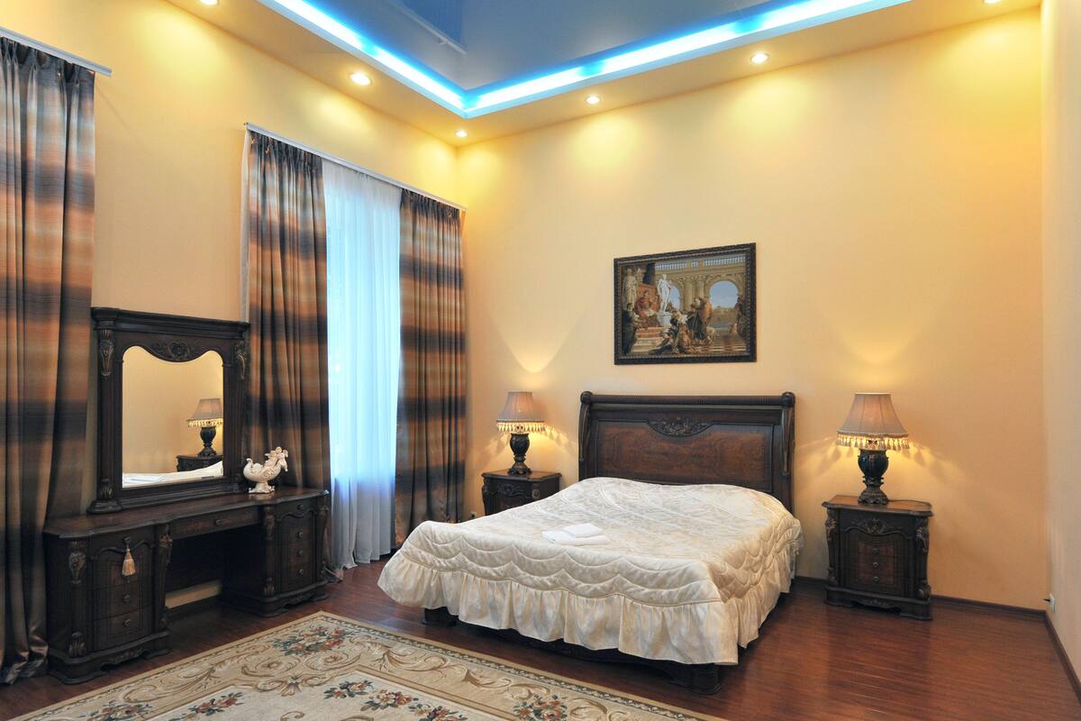 A bedroom with a large bed, a dresser, a mirror, and two bedside lamps.