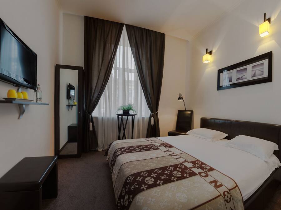Habitación de hotel con cama, televisión, repisa con artículos de aseo, mesita de noche y ventana con cortinas.