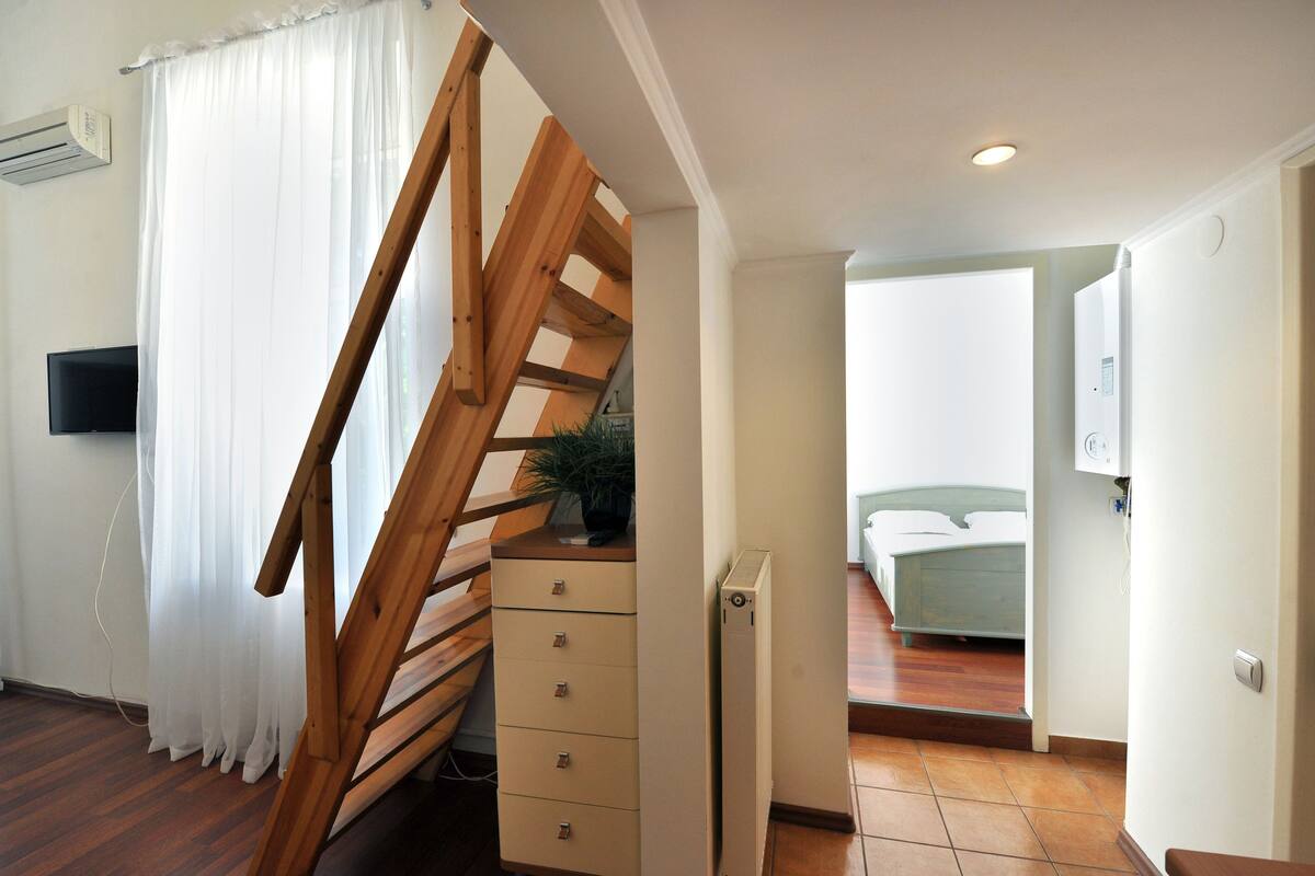 A room with a wooden staircase, a bed, a radiator, and a television.