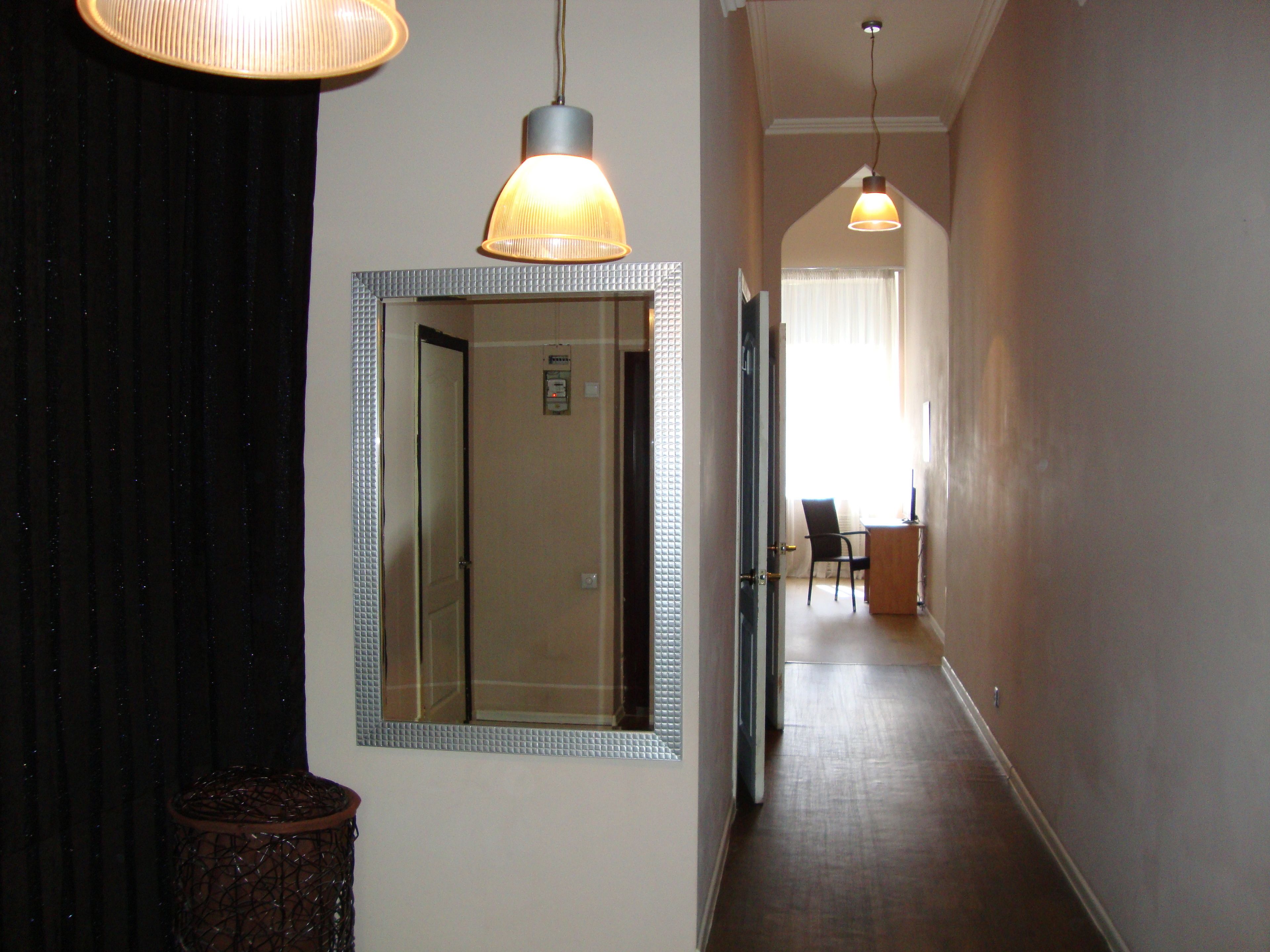 A hallway with a mirror, a door, and a desk with a chair.