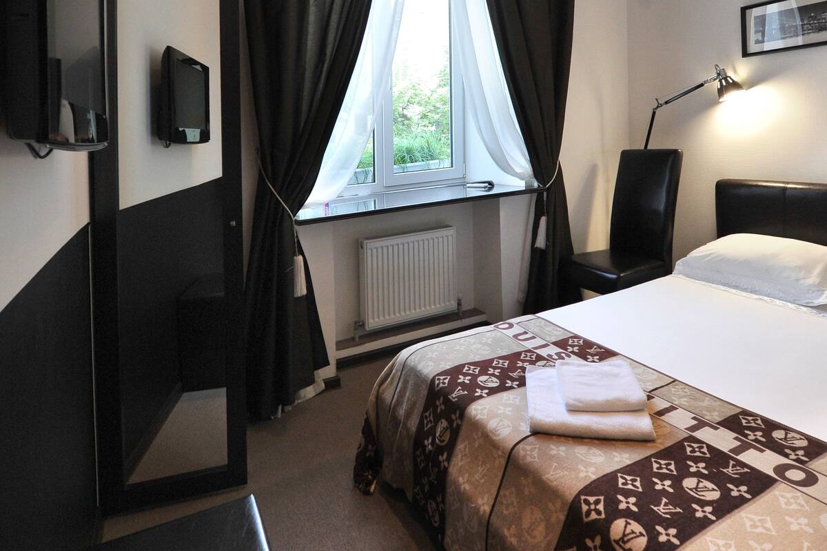 A hotel room with a bed, a desk, a chair, a TV, and a window with curtains.