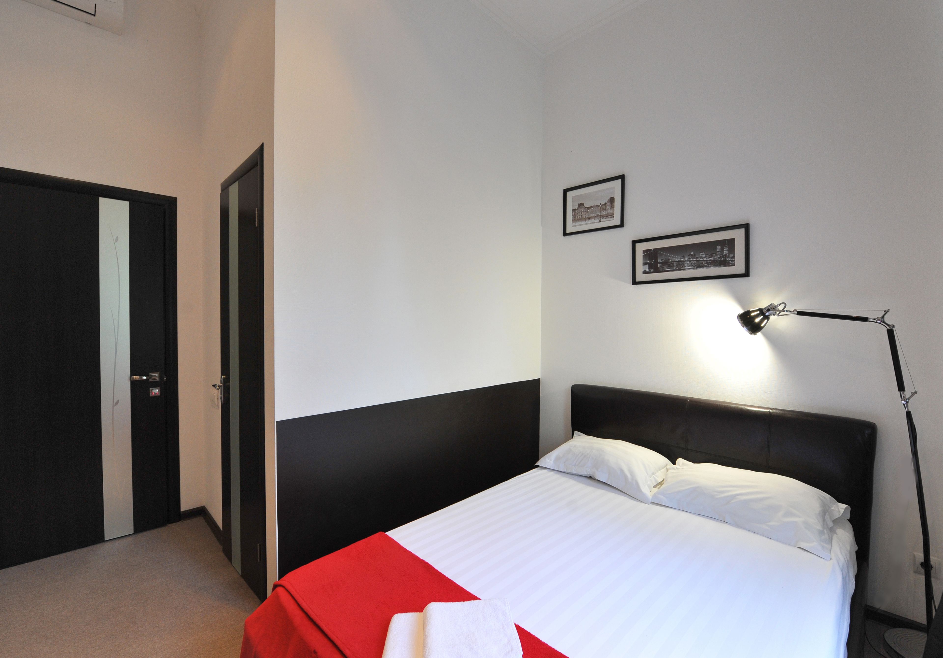 Une chambre d’hôtel avec un lit, un bureau, une chaise, une lampe et une porte.