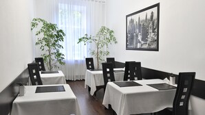 A dining area with white tables and chairs, a cityscape painting on the wall, and two potted plants. - Reno (Odesa)