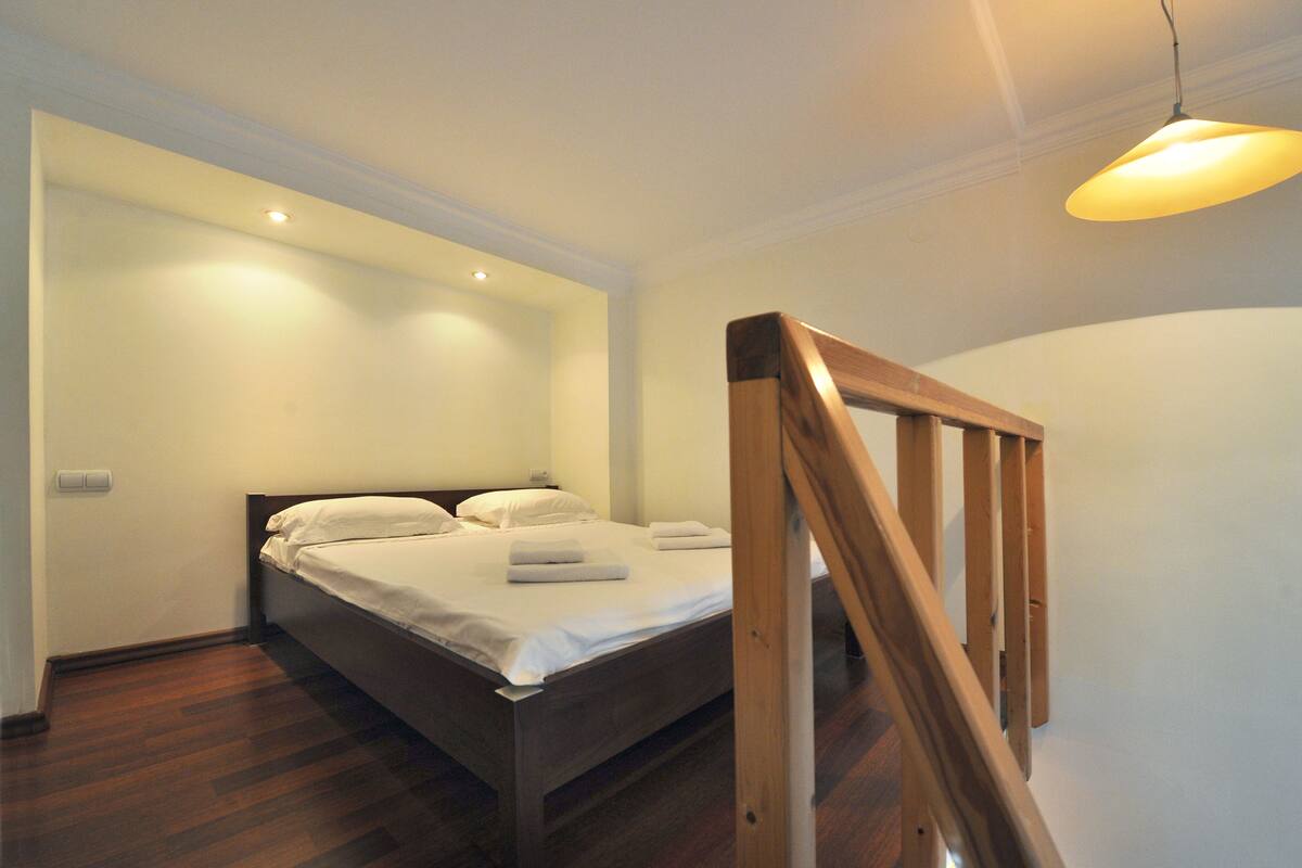 A bedroom with a wooden bed, white linens, and a wooden staircase.