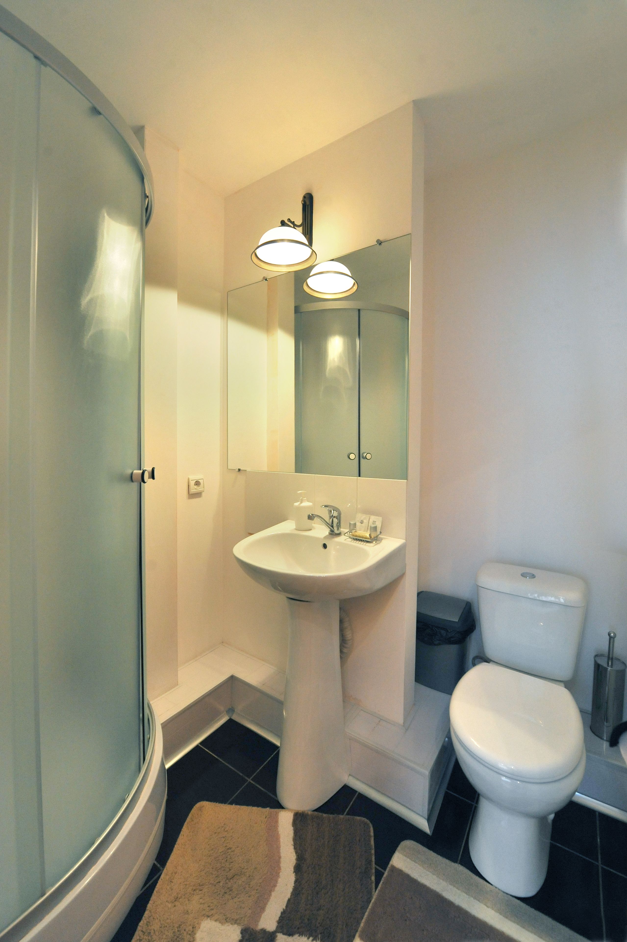 Een badkamer met een douchecabine van glas, een wastafel op een voetstuk, een toilet en een spiegel boven de wastafel.