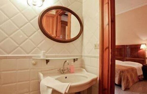 A bathroom with a sink, mirror, and a bed visible through an open door. - La Maison de Marta (Rome)