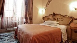 A hotel room with a bed, a nightstand, a lamp, and a window with curtains. - La Maison de Marta (Rome)