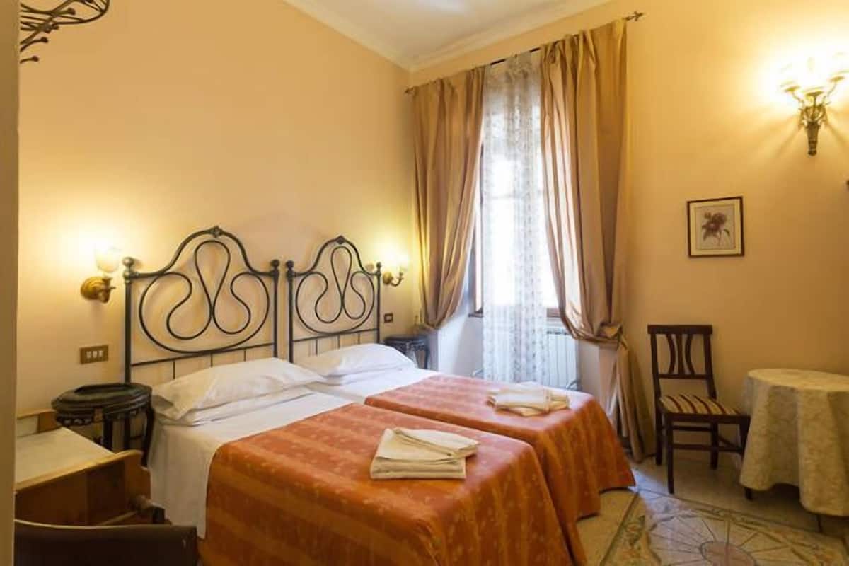 A hotel room with a double bed, two single beds, a chair, a small table, and a window with curtains.
